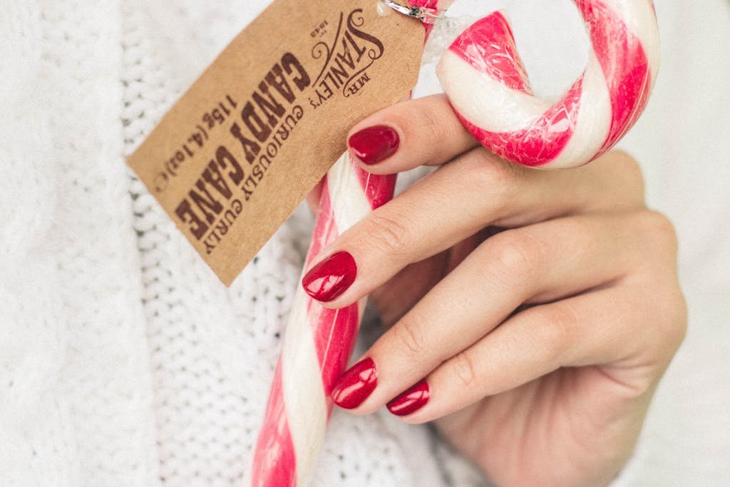 A hand with red nail polish holding red and white candy cane, perfect for Christmas