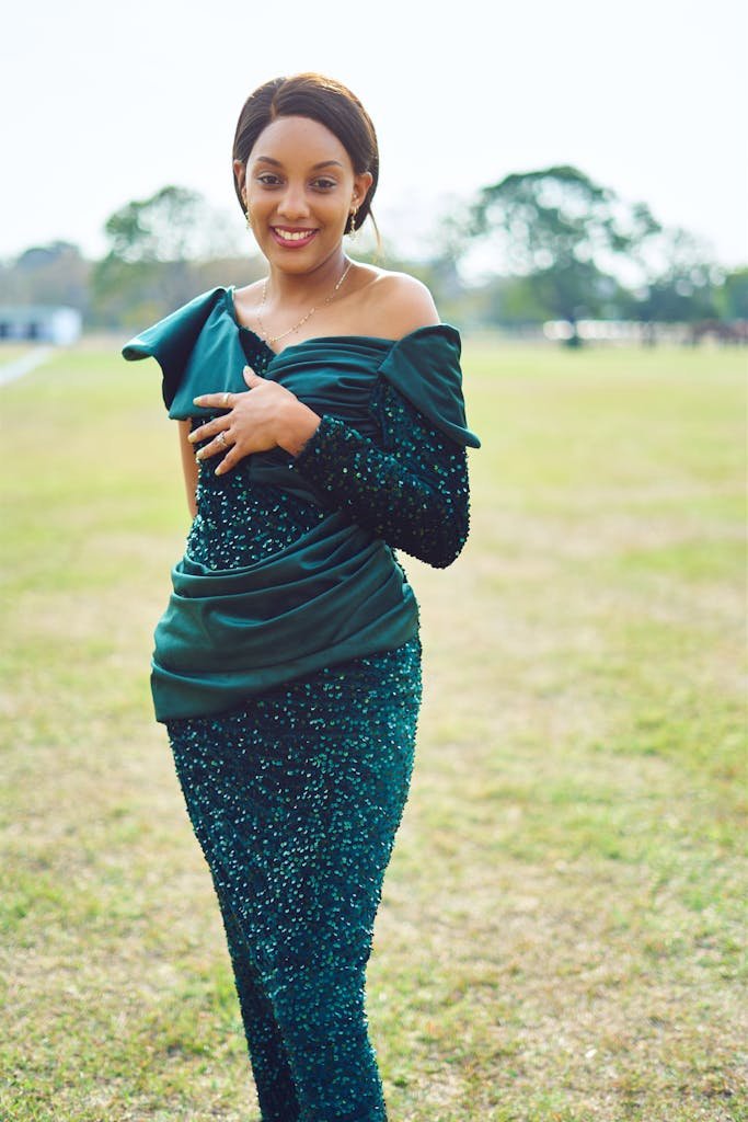 A woman in an elegant emerald green dress smiles in an outdoor setting, exuding confidence and charm.