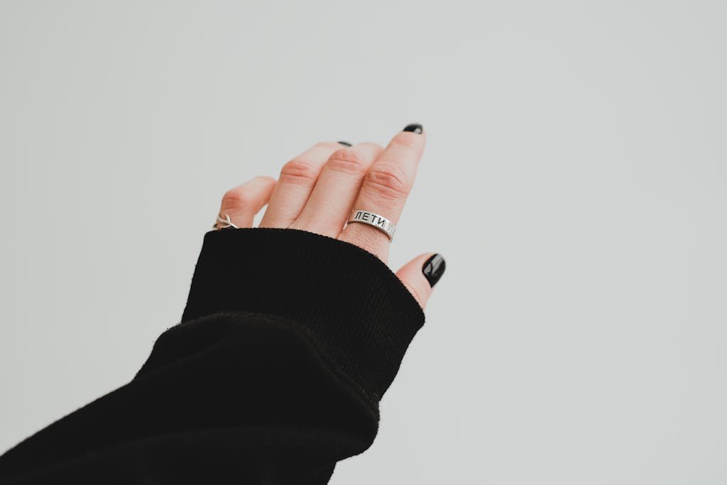 Aesthetic close-up of a hand with black nails, rings, and a cozy sweater sleeve.
