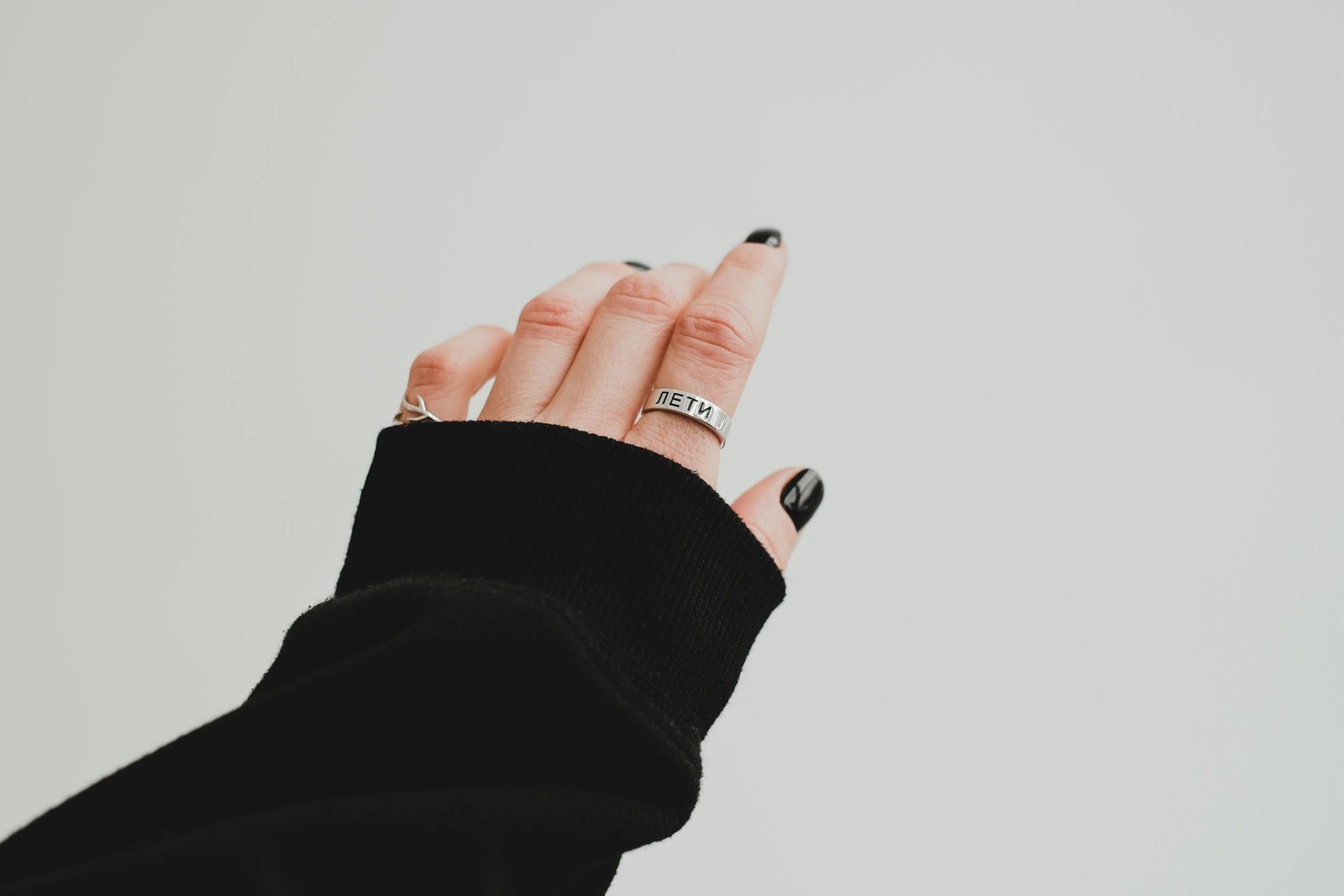 Black fall nail colors 2026 — hand with black manicured nails, rings, and a cozy sweater sleeve