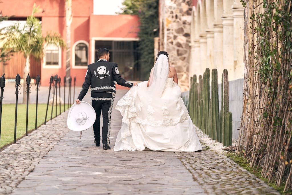 Bride and groom in traditional Mexican outfits walking in a cobblestone courtyard.