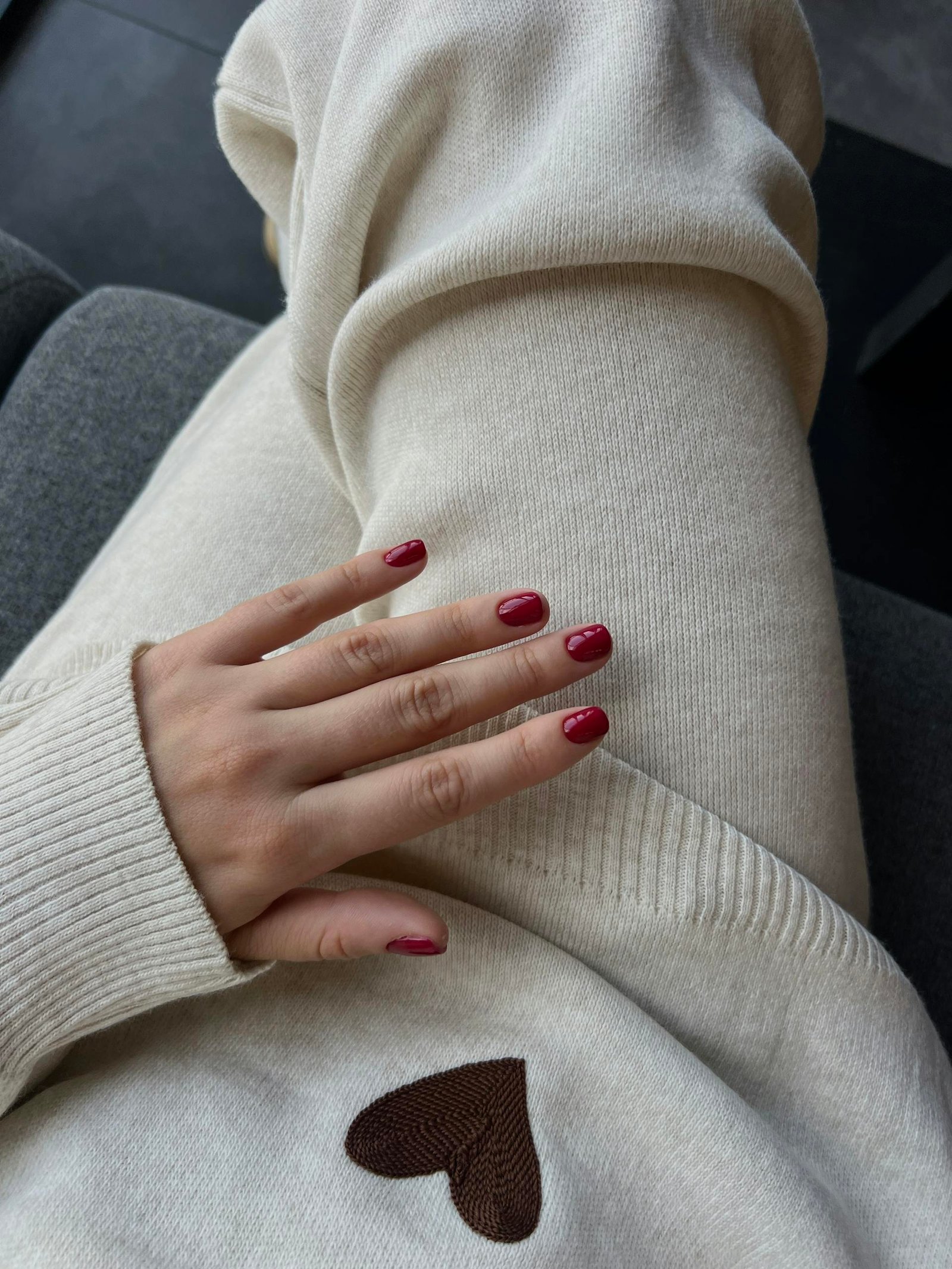 Close-up of a cozy outfit with burgundy nails and heart detail.