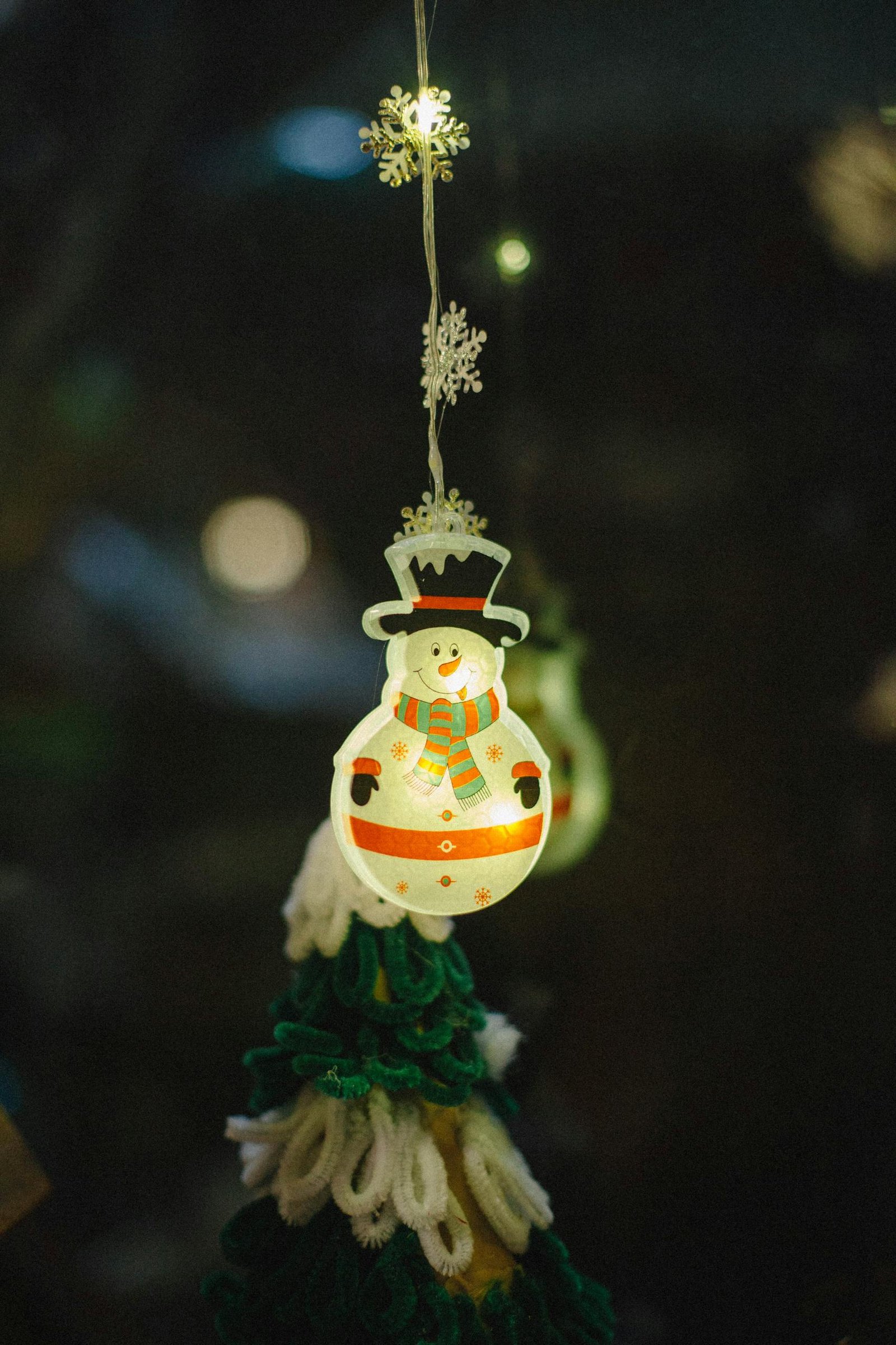 Close-up of a glowing snowman ornament hanging with bokeh lights in a festive setting.