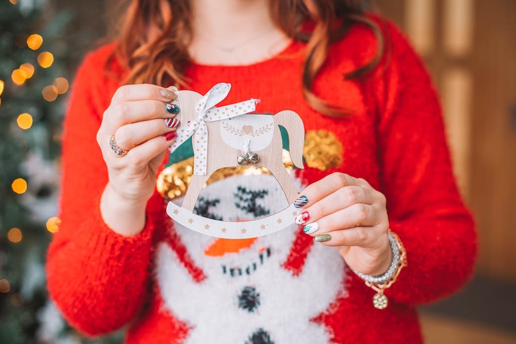 Close-up of a woman in a festive sweater holding a Christmas ornament, showcasing her nail art.
