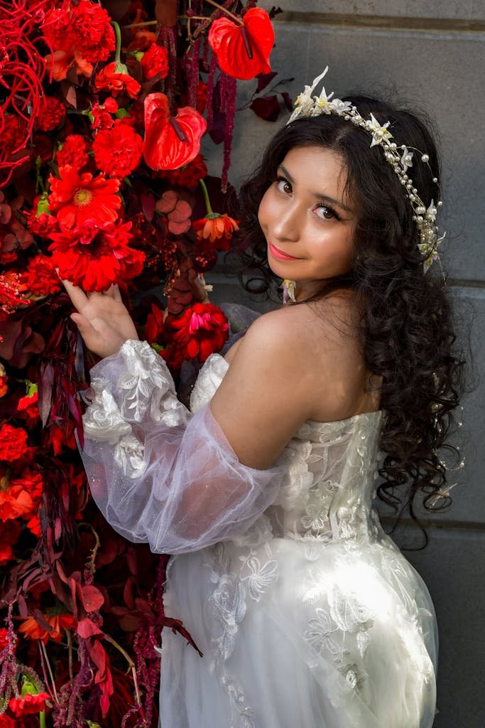 Elegant woman in a white bridal gown posing against a vivid red floral display.