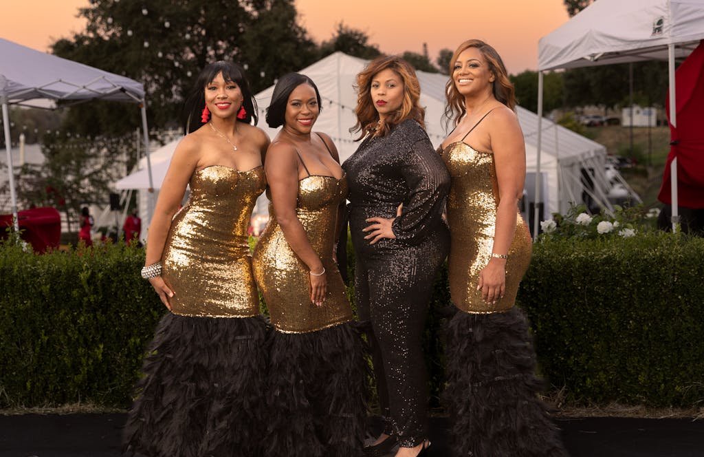 Glamorous outdoor event featuring women in sparkling gold dresses posing elegantly.
