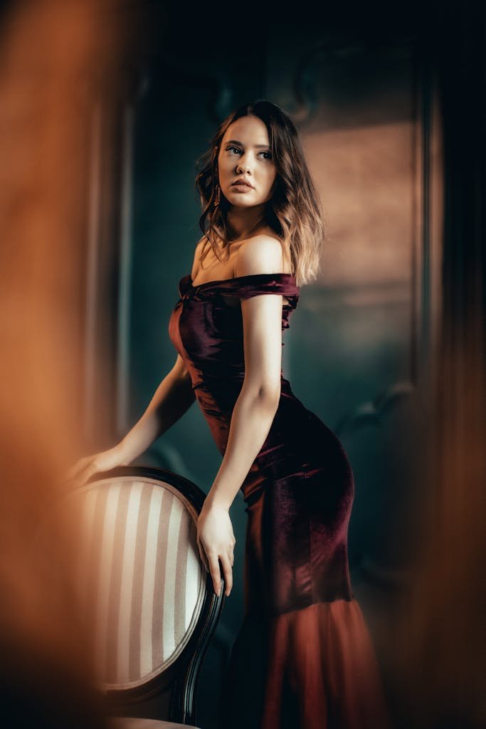 Portrait of a woman in a burgundy evening gown posing elegantly in a studio.