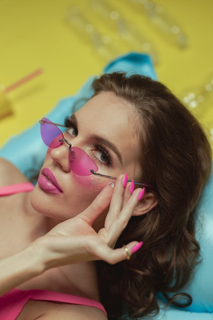 Stylish woman with pink sunglasses posing on yellow background, fashion concept.