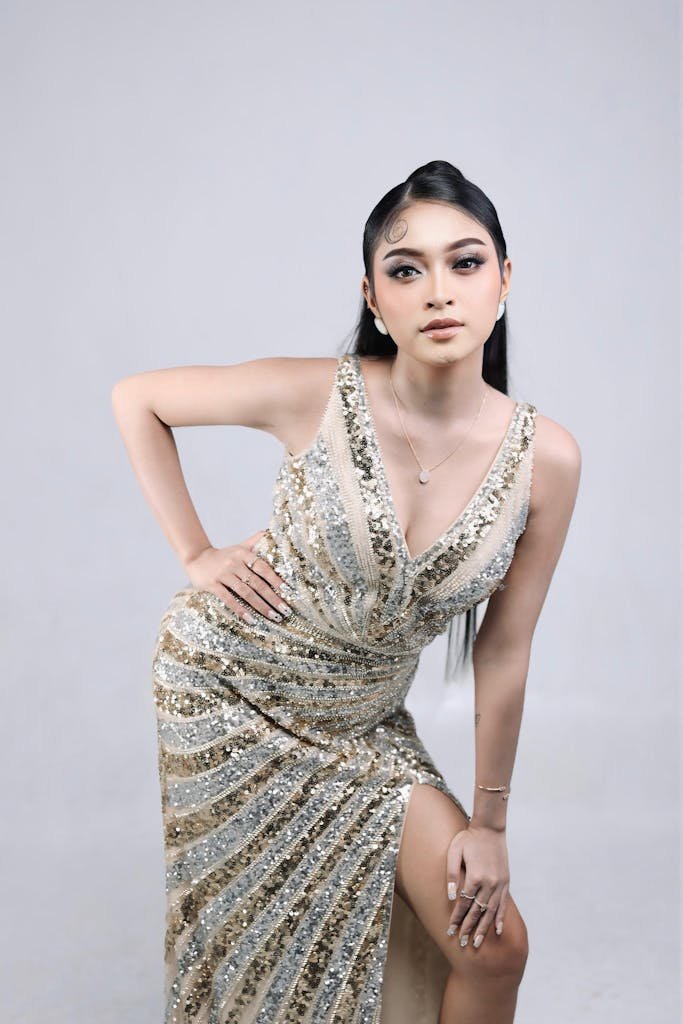 Stylish young woman posing in a glamorous sequin gown in a studio.