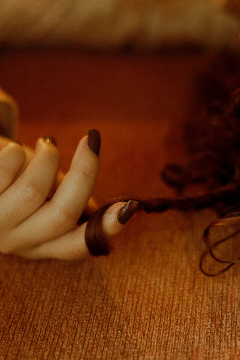 Close-up of a woman's hand with brown nail polish fondling curly brunette hair.
