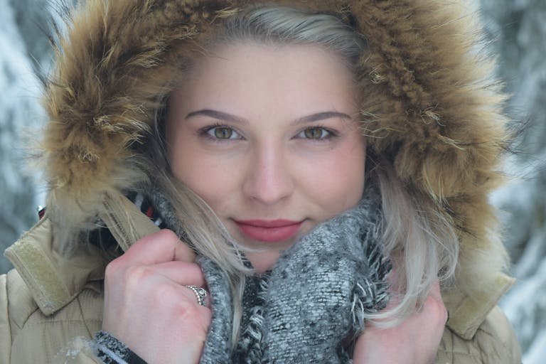 Close-up winter portrait of a woman in a fur hooded jacket with a scarf.