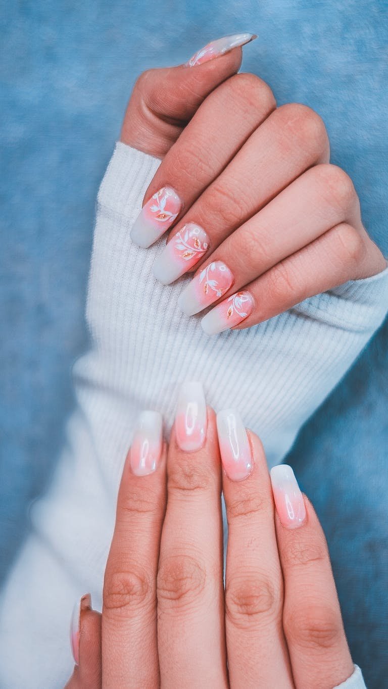 Close-up of hands showcasing elegant gradient nail art with floral designs.