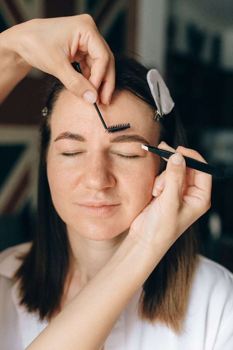 Close-up of a woman having her Professional eyebrow lamination process showing fluffy, lifted brows being groomed with a brush.eyebrows groomed with a brush and tweezers.