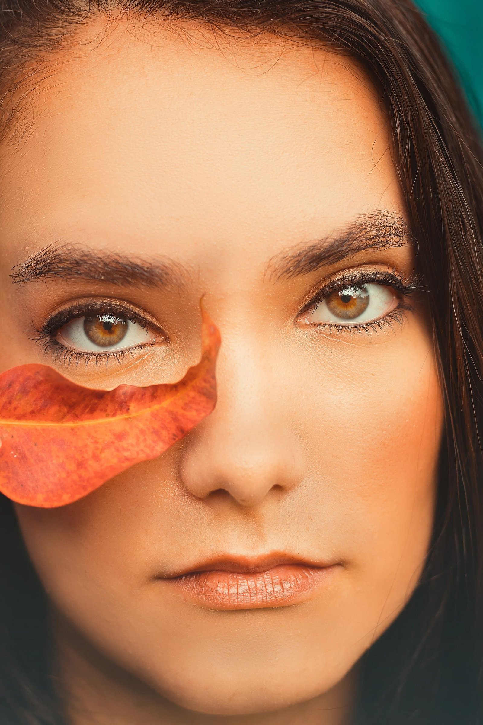 A captivating close-up portrait of a woman, highlighted by an orange leaf, blending natural beauty with earthy tones.