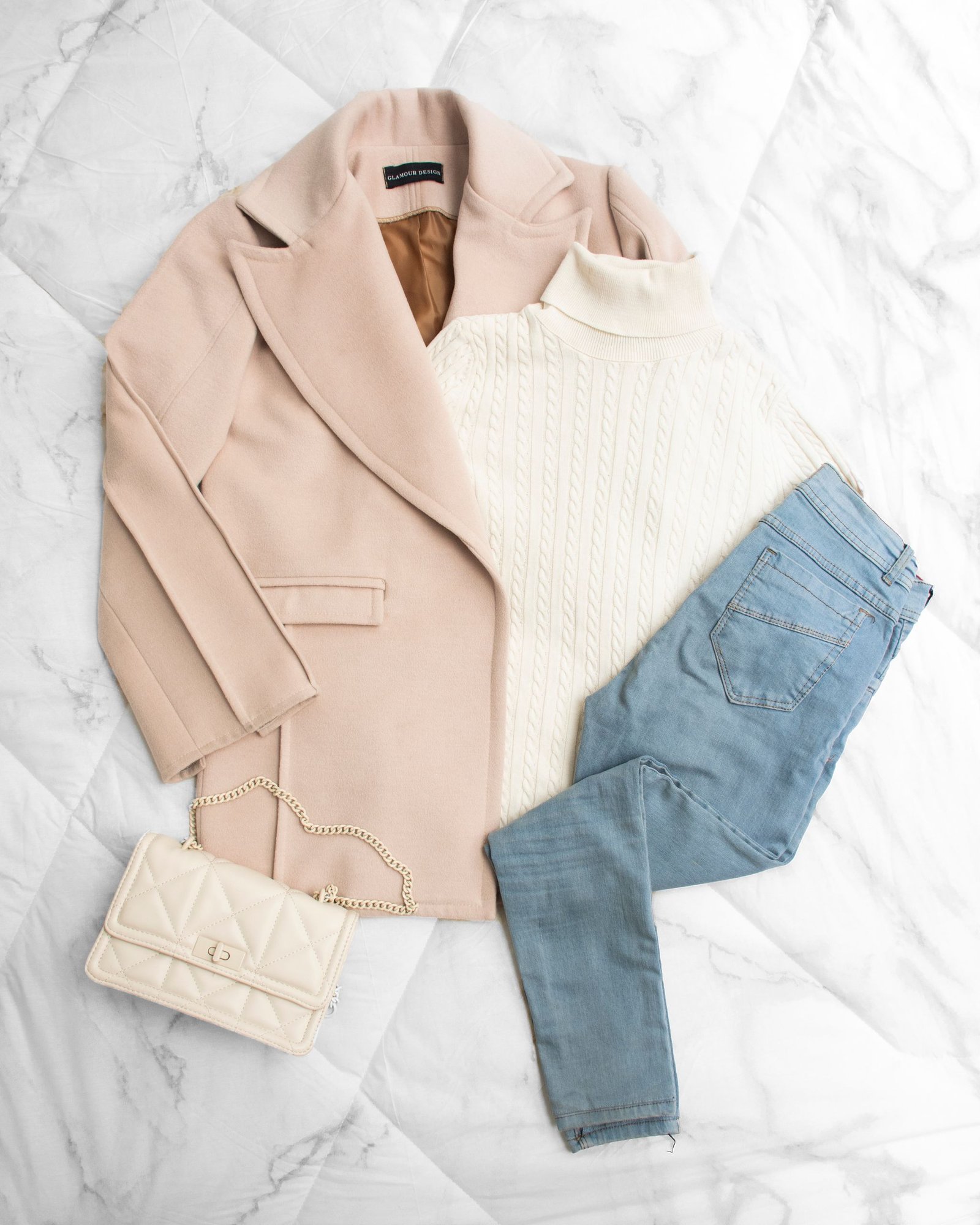 Chic flat lay of a winter outfit with beige jacket, turtleneck, denim pants, and shoulder bag.