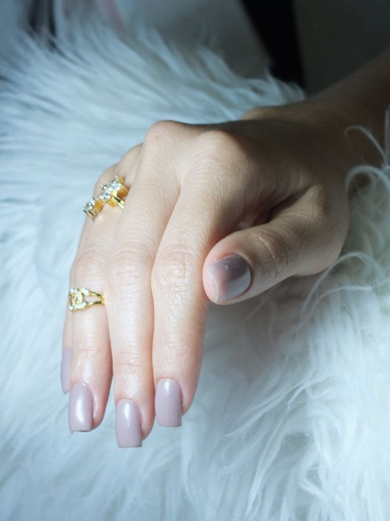 Close-up of a female hand with manicured nails and gold rings on a fluffy white background.