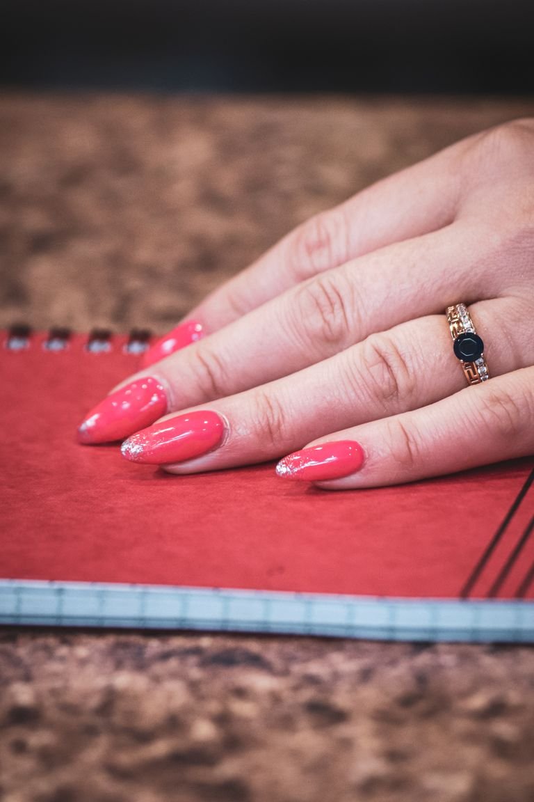 Close-up of a hand with pink manicured nails and a ring resting on a notebook.