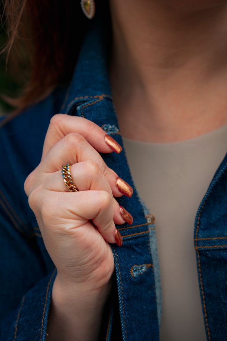 Close-up of a woman's hand in denim with copper nails, capturing fall fashion trends.