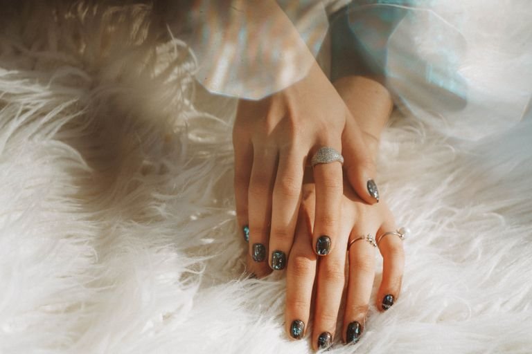 Close-up of a woman's hands wearing rings and nail art, resting on white faux fur.
