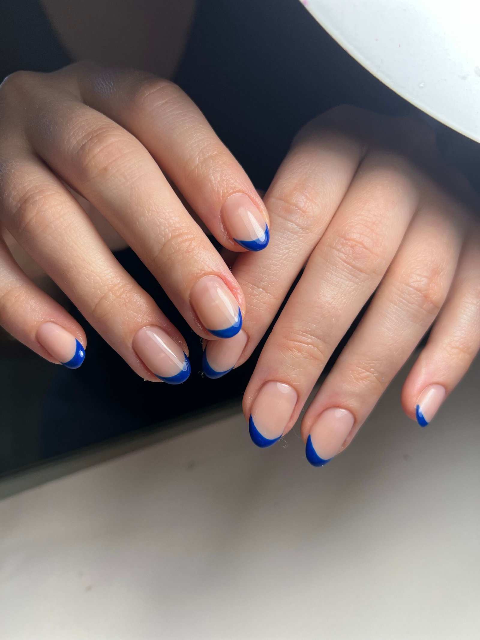 Close-up of a woman's hands with blue-tipped manicure under soft light.