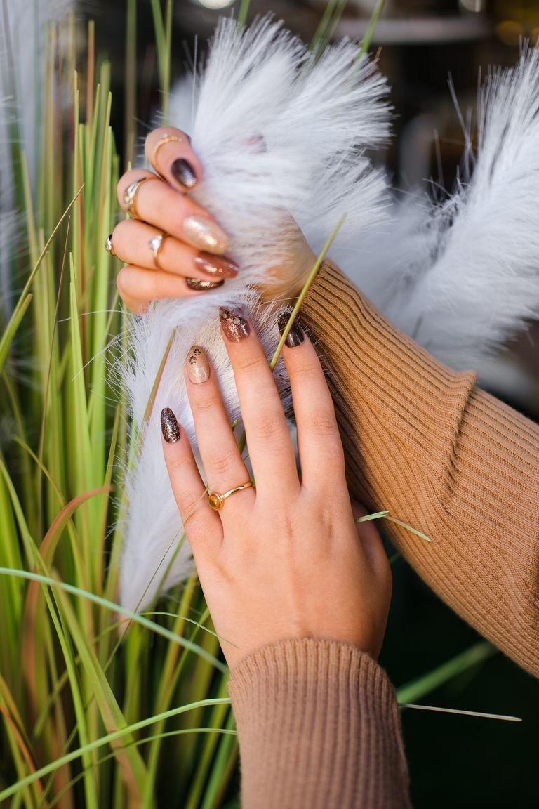 Close-up of elegant hands with nail art touching ornamental grass, showcasing fashion and beauty.