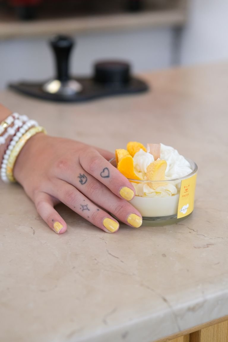 Tattooed hand with yellow nails holding a creamy dessert, adorned with orange fruit slices.
