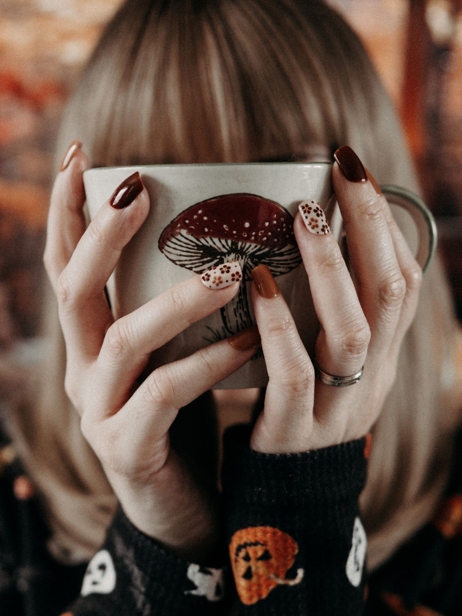 Warm autumn vibes with a mug featuring mushroom art, held by a person with stylish nails.
