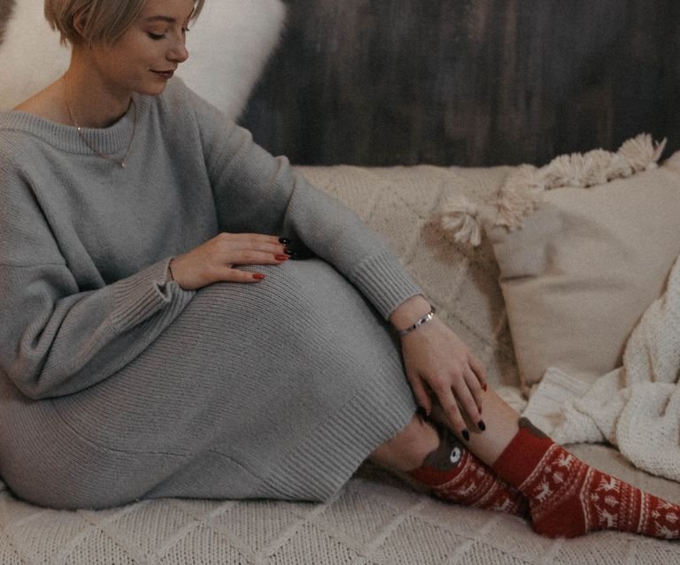 Woman in a cozy indoor setting wearing a knitted dress and festive socks.